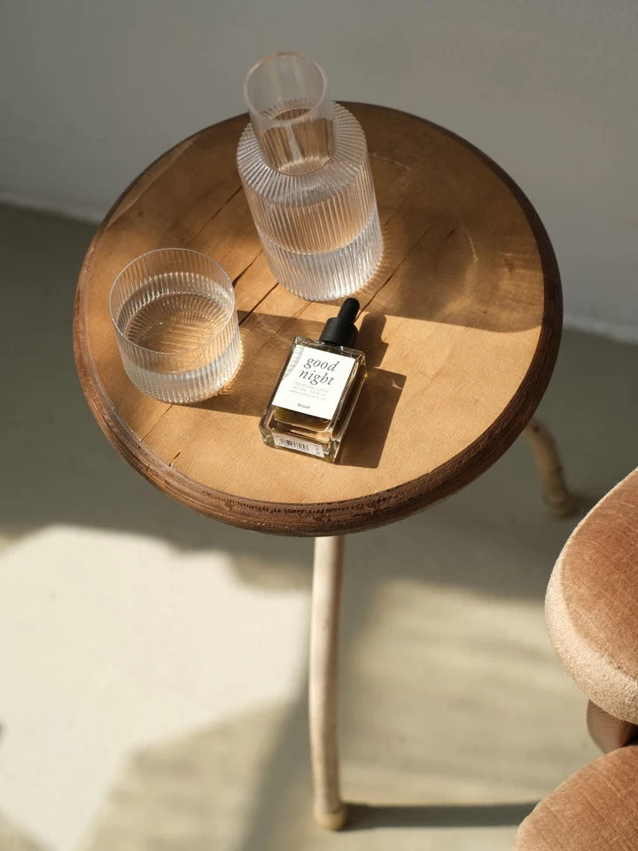 KRUUT Good Night Tinktur auf einem kleinen Holztisch mit zwei geriffelten Wassergläsern bei natürlichem Licht
